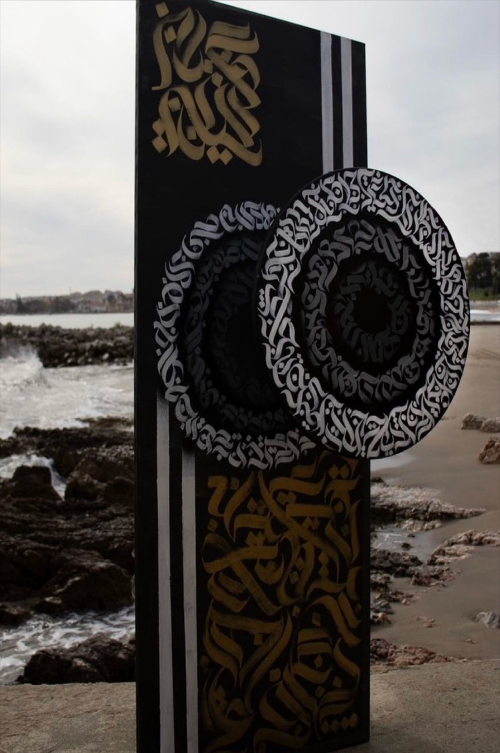 Painel com círculos de caligrafia fotografado na praia