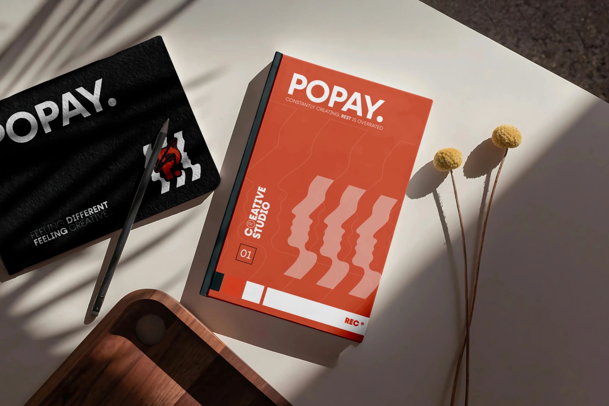 Caderno preto e livro laranja Popay sobre uma mesa clara com sombras